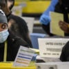 Two black ballot counters in Philadelphia. On the left, a wide-eyed woman with a mask and a mouse wool cap and on the right a male holding up a yellow ballot.