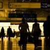 People are seen walking through an airport terminal in dark lighting.